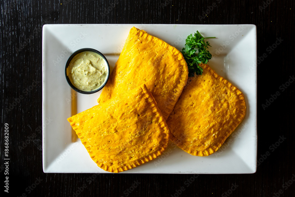 Ταπετσαρία Overhead view of golden baked Jamaican beef patties on a white plate with cilant