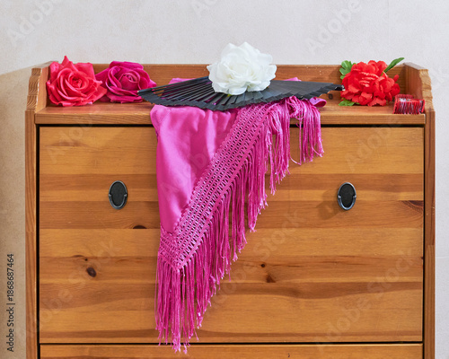 Vibrant pink flamenco shawl, roses, and fan on wooden chest