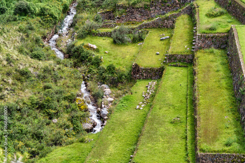 Natural mountain stream flowing through lush green vegetation at the Pisac archaeological complex in the Sacred Valley of Peru.
