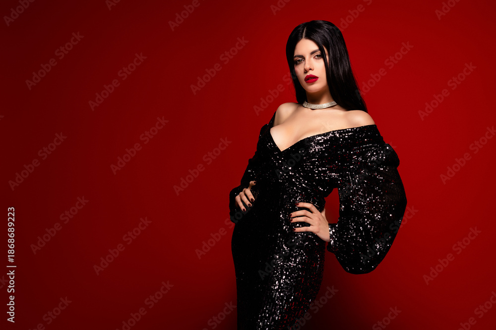 Obraz premium Portrait of a glamorous woman in an elegant sequined dress posing confidently on a vibrant red background