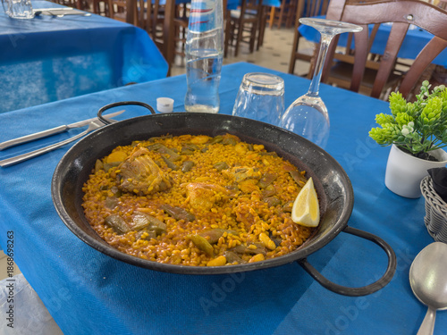 Photography Savoring authentic paella Valenciana: saffron-infused rice with tender chicken, green beans, and a zesty lemon wedge, served in a traditional pan at a sunny Mediterranean restaurant