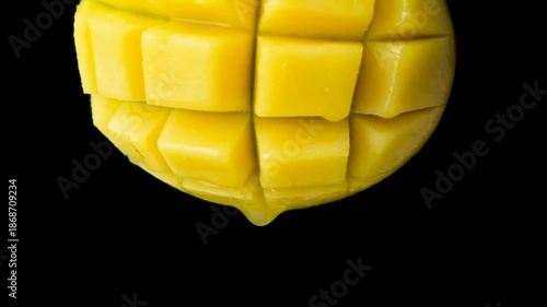 Mango juice slowly dripping from fresh fruit, black background, macro