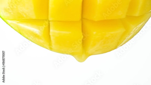 Mango juice slowly dripping from fresh fruit, white background, macro