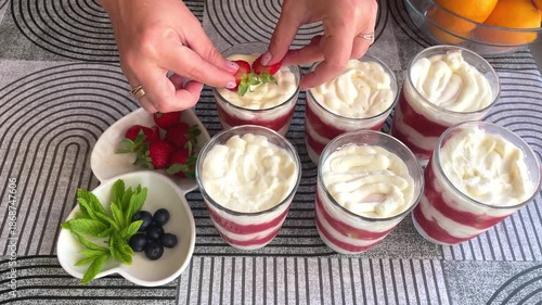 Hands decorating strawberry tiramisu with berries and mint. 4K horizontal footage shows female hands arranging strawberries, blueberries, and fresh mint on a dessert in a glass