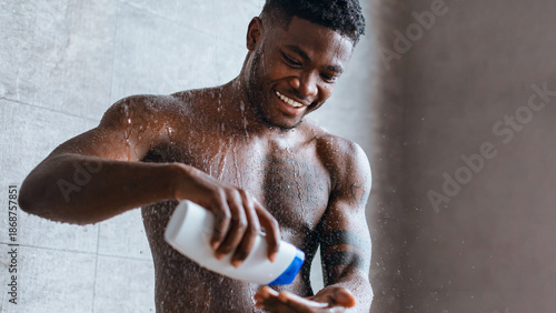 Fotografija A man is in the shower, holding a bottle of shampoo while smiling