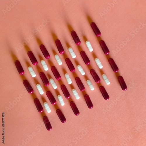 Foto medicamentos en cápsulas blancas y rojas colocadas en   diagonal hacia la izquierda en bandas alternas de colores sobre fondo naranja