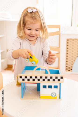 Little girl playing with small wooden car in the kindergarten