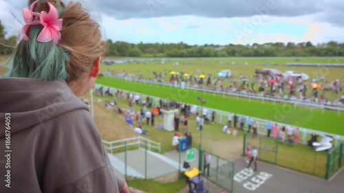 A young girl stands in the grandstand, intently watching racehorses gallop past at high speed. A dynamic scene capturing the excitement of equestrian sports, betting, and spectator events