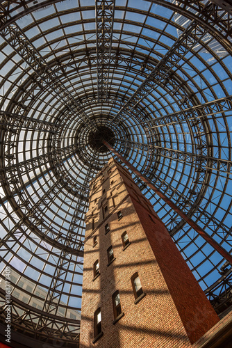 Photograph of the historic Coop's Shot Tower in Melbourne, Australia, encased under a massive modern glass dome at Melbourne Central Shopping Centre. A stunning contrast of old-world architecture 