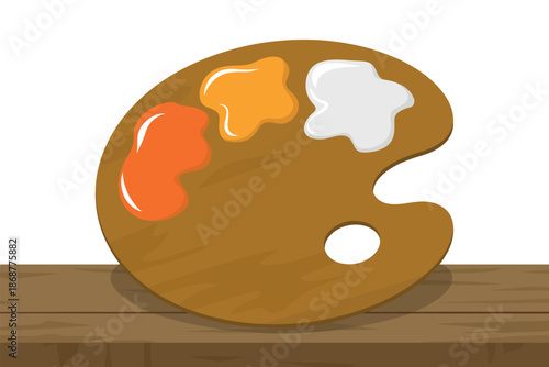 A painter's palette with orange, yellow, and white paint on a wooden table