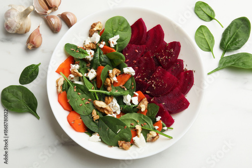 Delicious salad with beetroot, spinach, cheese, walnuts and carrot on white table, top view © New Africa