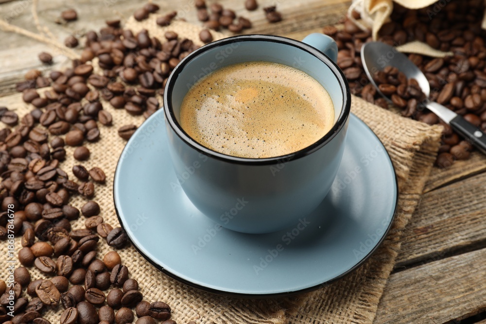Fototapeta premium Aromatic coffee in cup and beans on wooden table, closeup