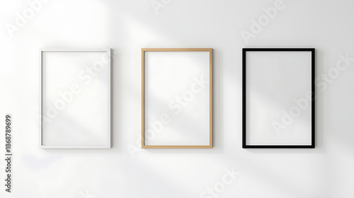 Minimalist mockup of three vertical empty picture frames on a white wall a white frame on the left, a light wood frame in the middle, and a black frame on the right. The scene benefits from soft natur