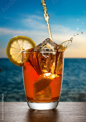 Tall glass of iced tea with a lemon slice, filled with ice cubes, against a vivid blue sky and ocean background.