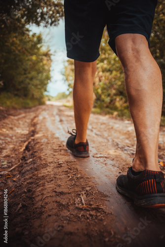 Low-angle close-up of legs walking on a muddy rural trail with deep ruts, outdoor adventure and endurance concept.