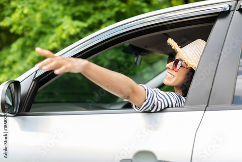 Wallpaper Mural Happy middle-eastern young woman in stylish summer hat and sunglasses enjoying car trip, sitting at front seat in nice auto, looking through window, touching air with hand, side view Torontodigital.ca