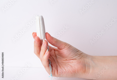 Hand holds a white tampon with blue string against a plain background