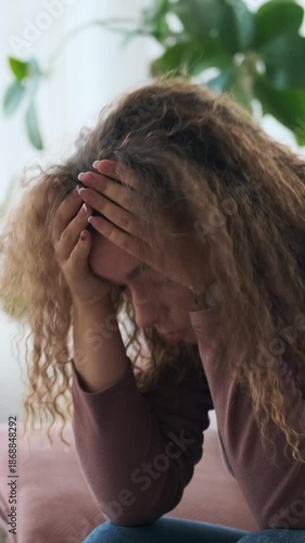 Vertical video of a sad young woman feeling anxious and depressed. She is sitting on a sofa at home, suffering from mental health problems.
