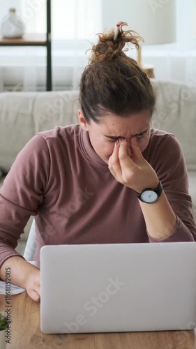 A tired and frustrated young woman feels overwhelmed by a work deadline on her laptop at home. Vertical video.