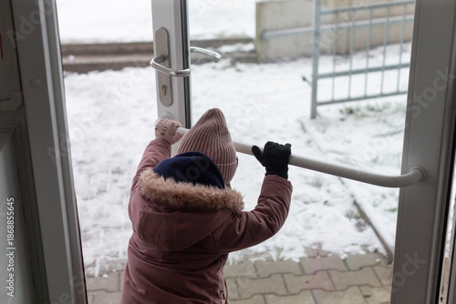 child opening glass door handle with mittened hand, focused small gesture of independence at residential entrance,