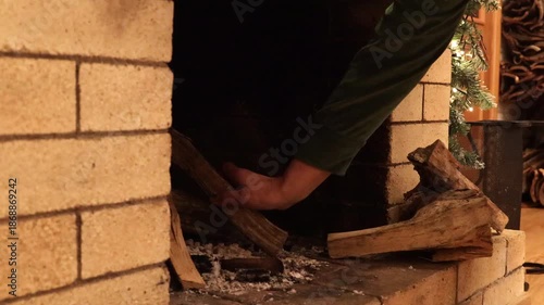 Close-up of hands placing firewood into a fireplace and lighting the fire. Cozy home atmosphere, warmth and comfort, winter evening concept, traditional heating, hygge lifestyle and relaxing mood