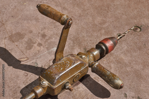 Vintage metal hand drill with wooden elements and visible wear. Traditional manual drilling tool representing craftsmanship, repair work, and historical technology.