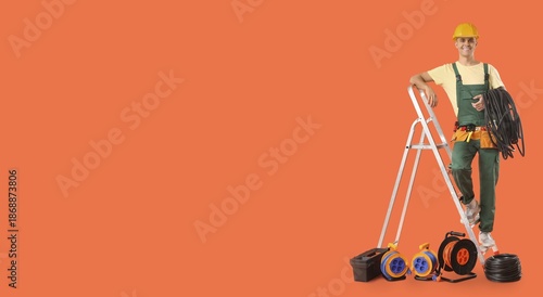 Slika na platnu Young male electrician with stepladder and equipment on orange background with s