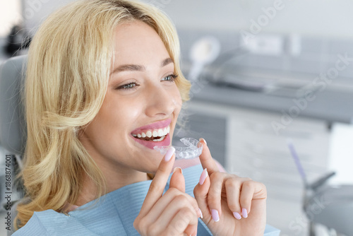 Wallpaper Mural Invisalign orthodontics, modern dentistry concept. Happy young attractive blonde woman holding invisible braces or trainer while sitting at dental chair, closeup portrait, copy space Torontodigital.ca