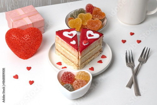 A dessert table features a slice of cake decorated with hearts, colorful candy, and wrapped gifts. Small hearts are scattered across the table. Items create a festive atmosphere