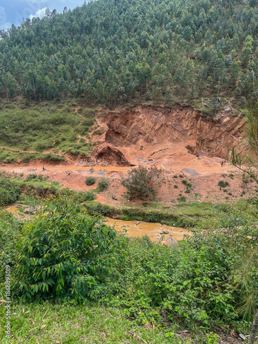 Panoramic view of Rwandan hills with many people working on a large area of red tilled soil for planting.