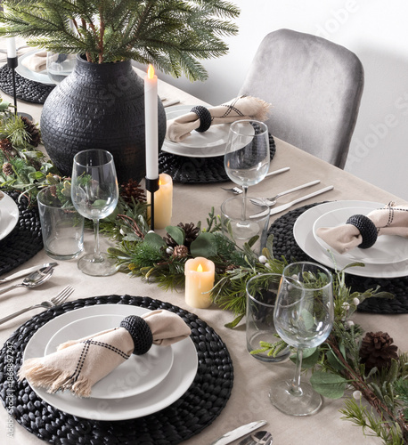 Bild auf Leinwand Festive New Year's Eve dinner table adorned with a pine garland centerpiece, decorative woven black placemats, elegant white dishes with fringed napkins and candles