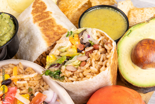 A cut open Mexican burrito with an avocado and dipping sauce
