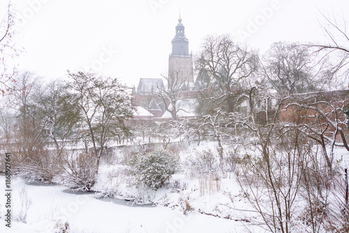 City wall of Zutphen, The Netherlands, with iconic medieval historic buildings in Hanseatic town during winter with tower of the Walburgiskerk rising above in blizzard snowstorm