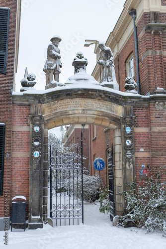 Stone statues marking the entrance of a courtyard in the city center of historic medieval town covered in snow. Winter wonderland urban scene
