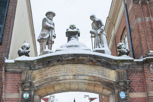 Stone statues marking the entrance of a courtyard in the city center of historic medieval town covered in snow. Winter wonderland urban scene