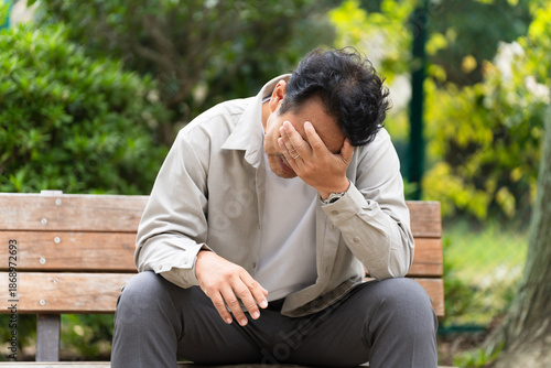 ベンチを座りながら落ち込んでいるミドル男性　ライフスタイルイメージ