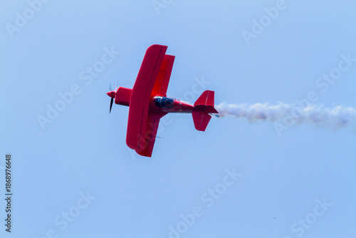 red biplane in flight trailing smoke