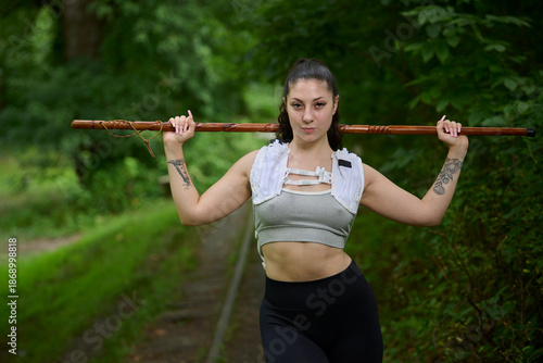 Beautiful young brunette female hiker pauses along a rail trail - holding carved walking stick