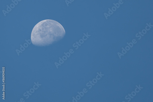 Fotografie Daytime moon phase with visible craters against a solid blue background, perfect for use as a minimal wallpaper