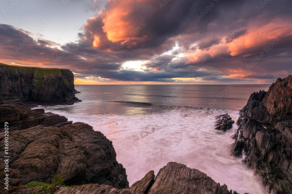 Obraz premium Dramatic Coastal Sunset Over Rugged Cliffs With Pink Clouds and Calm Sea