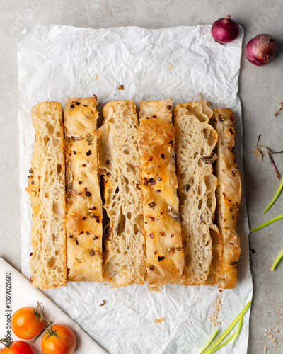 overhead view of slices of onion and scallion focaccia on parchment paper, top view of airy bubbly onion focaccia on a cement countertop