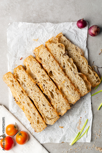 overhead view of slices of onion and scallion focaccia on parchment paper, top view of airy bubbly onion focaccia on a cement countertop