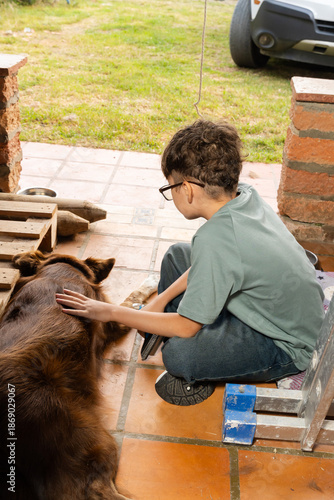 Young person petting large dog on tiled porch beside brick columns and yard