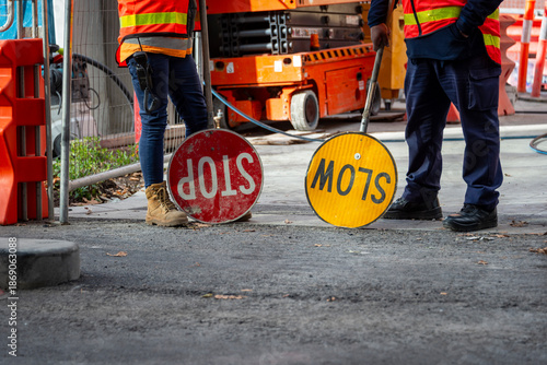Two traffic controllers, one with a slow sign, one with a stop sign, work boots and safety vest construction site