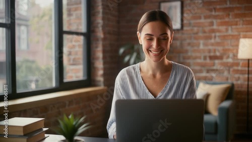 Contented young woman engaging with her laptop in a sunlit, modern home office, symbolizing the ease and productivity of remote work and digital learning