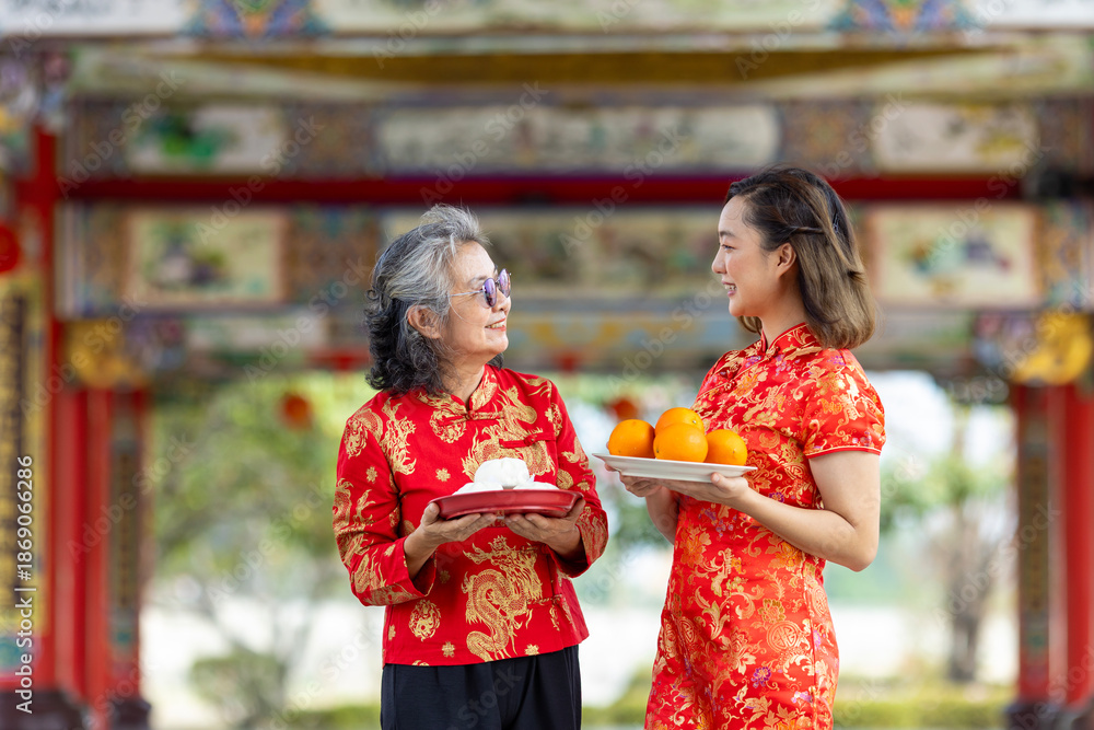 Obraz premium Asian woman with senior mother in red cheongsam qipao dress is offering food to ancestral god inside Chinese Buddhist temple during lunar new year for best wish blessing and good luck