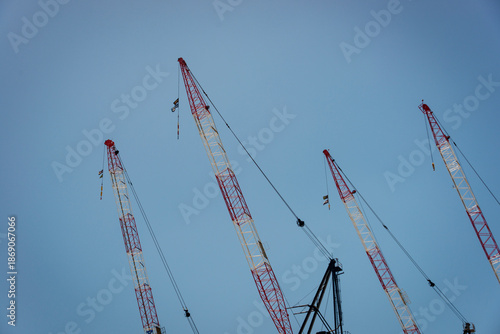 four construction cranes, red and white, against a clear blue sky, horizontal