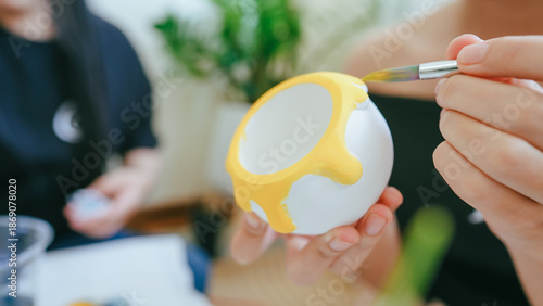 Close-up of a person painting a ceramic cup with yellow acrylic paint during a DIY arts and crafts activity at home or art workshop.