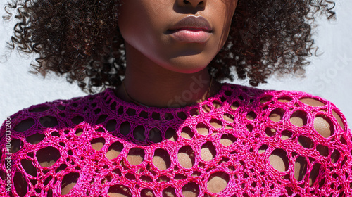 A portrait of an woman with curly hair wearing a pink openwork top 