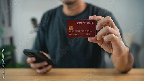 Φωτογραφία Man showing red credit card to camera while holding smartphone